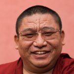 Een close up van een wijd grijnzende Chung Tsang Rimpoche.